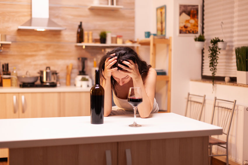Mujer tomando vino sola en su casa y soportando su cabeza en sus manos