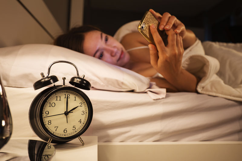 Mujer mirando su móvil, tarde en la noche en su cama